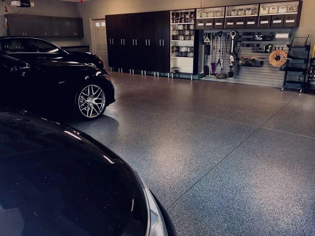 Two cars parked in a clean, organized garage with storage cabinets and shelves, featuring a durable epoxy floor coating and various household items neatly arranged along the back wall. - Floor Coating Specialist - Bradenton, FL