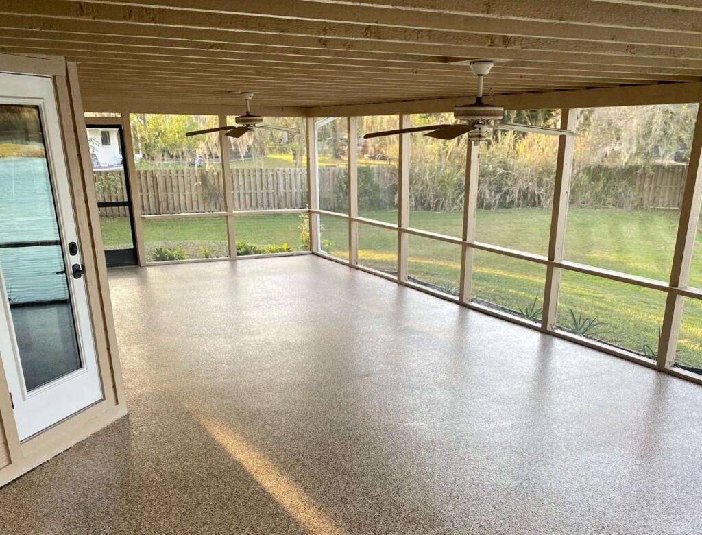Enclosed patio with screened walls, two ceiling fans, and polished concrete flooring, overlooking a grassy backyard with a wooden fence. - Floor Coating Specialist - Bradenton, FL