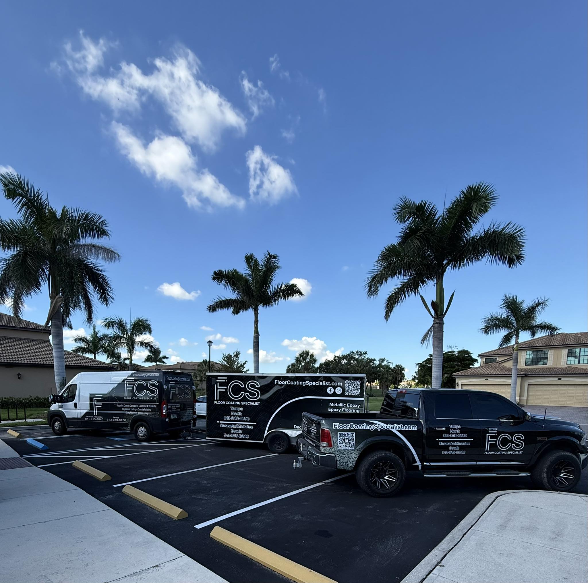 Two branded FCS company vehicles and a trailer are parked in a lot under palm trees on a clear day, with buildings visible in the background—ready to tackle your next polyaspartic floor coating or polished concrete flooring project. - Floor Coating Specialist - Bradenton, FL