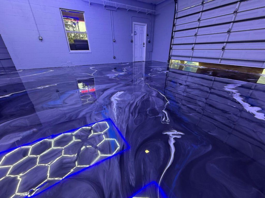 A garage interior with a glossy, marbled epoxy floor coating featuring blue and white swirls and embedded illuminated hexagon patterns. - Floor Coating Specialist - Bradenton, FL