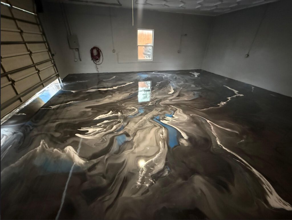 A garage with a shiny, marbled epoxy floor coating in shades of black, gray, and white, reflecting light from a window and a partially open garage door. - Floor Coating Specialist - Bradenton, FL