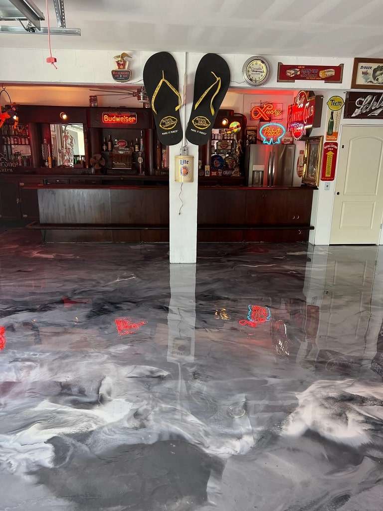 A garage bar with a glossy polyaspartic floor coating, neon signs on the walls, and two large flip-flop decorations mounted on a central pillar. - Floor Coating Specialist - Bradenton, FL