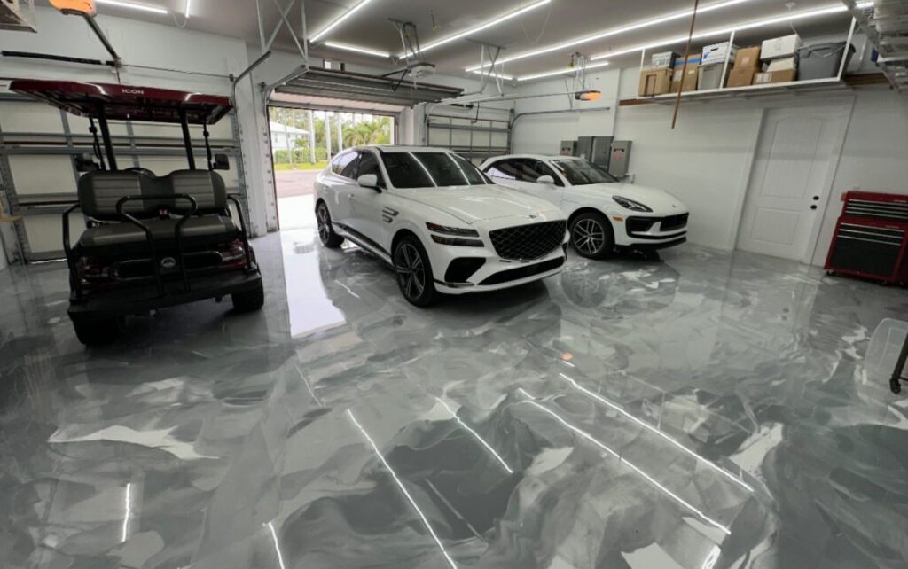 A garage with a glossy epoxy floor coating contains a red golf cart and two white cars, with shelves, boxes, and a tool chest visible in the background. - Floor Coating Specialist - Bradenton, FL