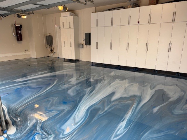 A clean garage interior features white cabinets and a glossy, blue and white marbled garage floor coating for a modern finish. - Floor Coating Specialist - Bradenton, FL