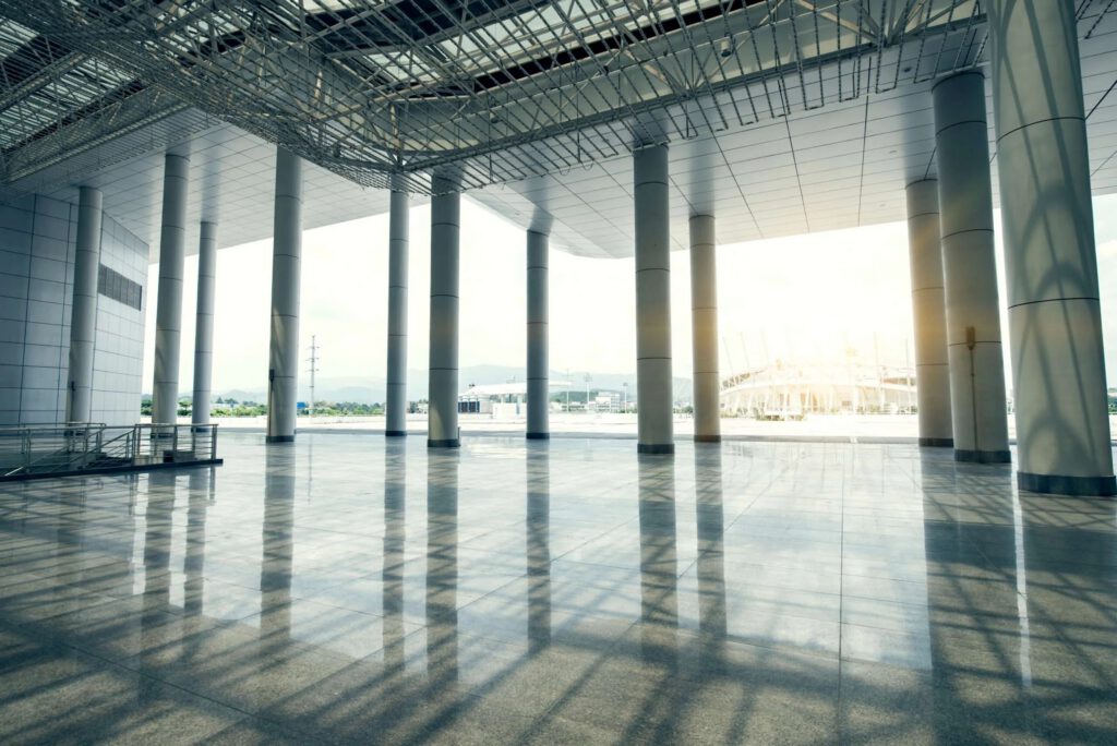 Spacious, empty airport terminal with tall columns and large glass windows, featuring a gleaming polyaspartic floor coating as sunlight streams in from outside. - Floor Coating Specialist - Bradenton, FL