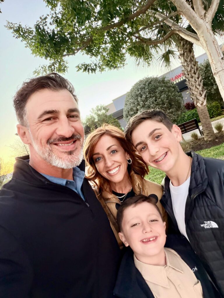 Four people, two adults and two children, stand outdoors smiling for a selfie in front of trees and a building with polished concrete flooring visible through the entrance. - Floor Coating Specialist - Bradenton, FL