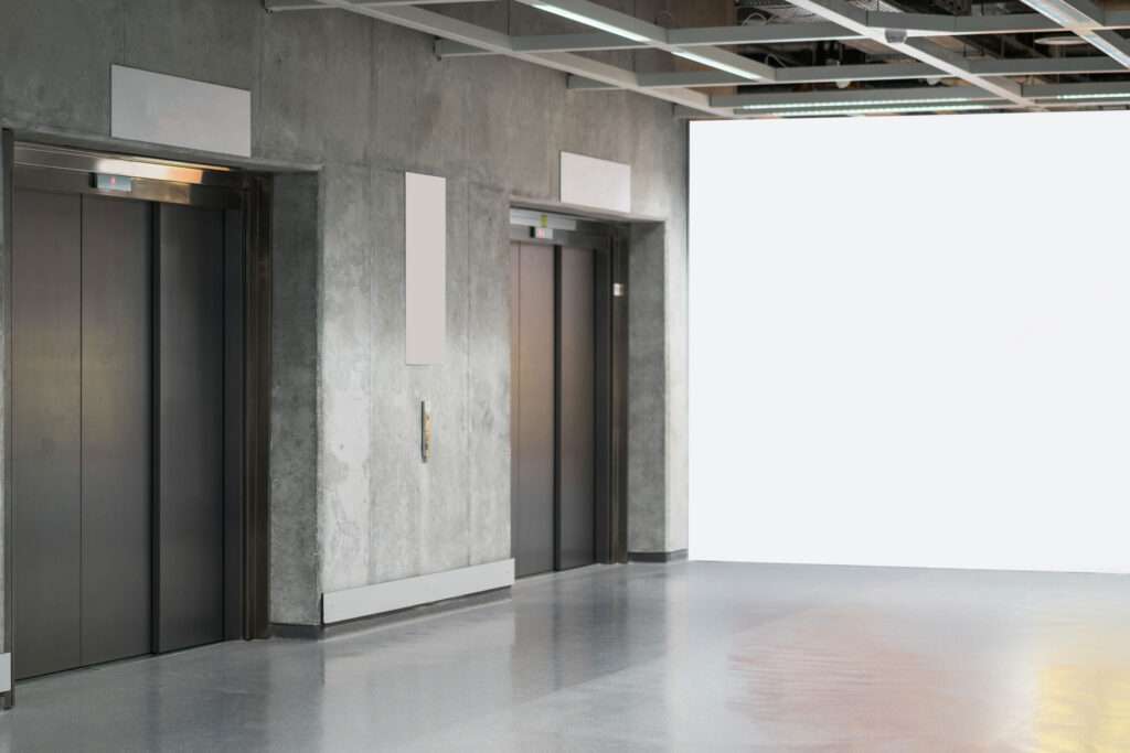 Two closed metal elevator doors in a modern building hallway with concrete walls and a bright, white-lit area on the right. - Floor Coating Specialist - Bradenton, FL