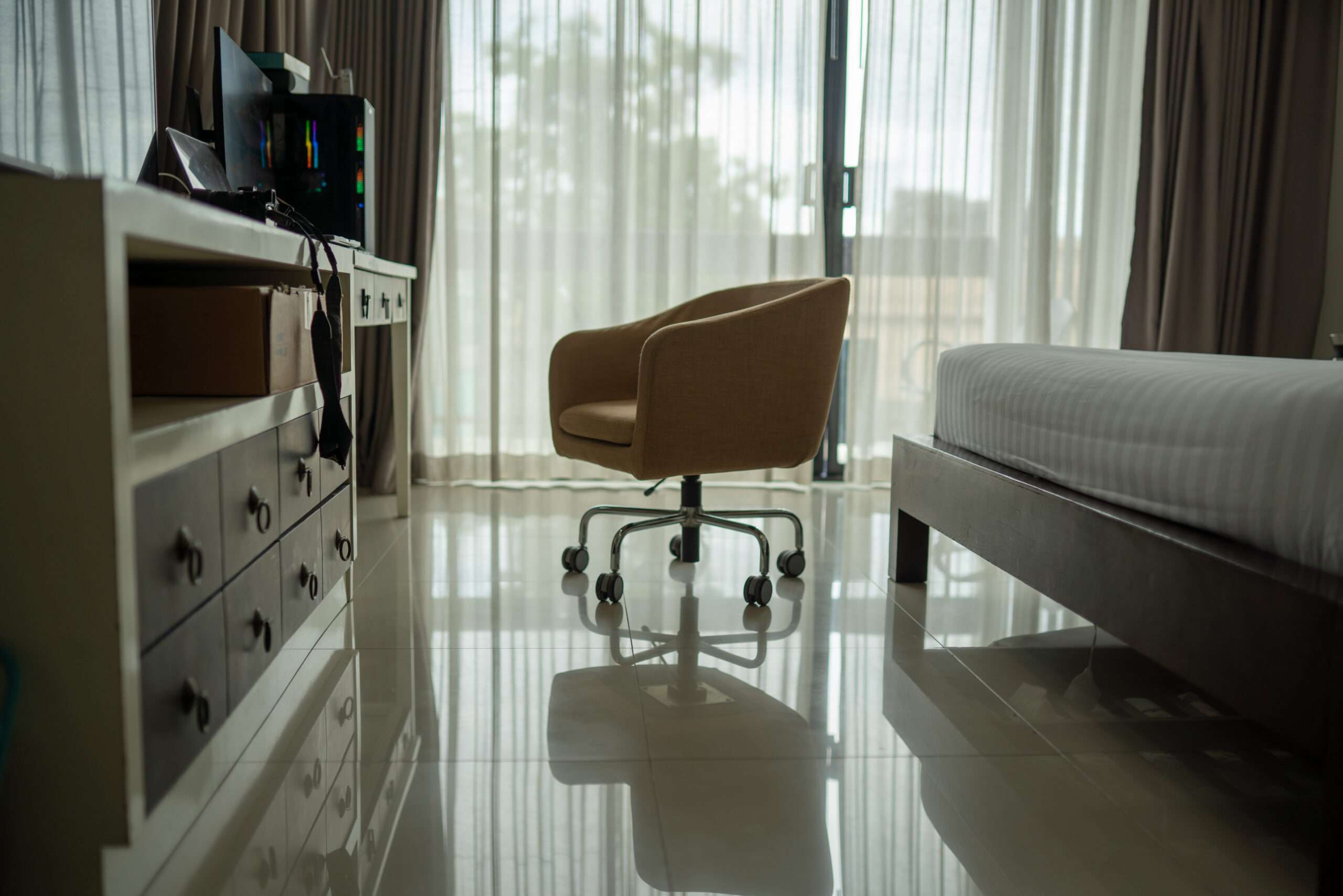 A swivel chair is positioned near a window in a modern, tidy bedroom with a bed, desk, and glossy tiled floor. - Floor Coating Specialist - Bradenton, FL