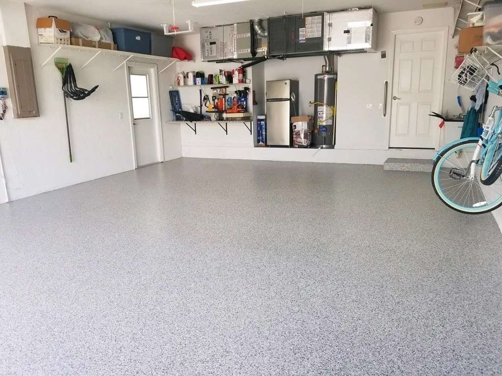 A clean, organized garage with a speckled floor, shelves holding various items, a bicycle, and utility equipment mounted on the back wall. - Floor Coating Specialist - Bradenton, FL