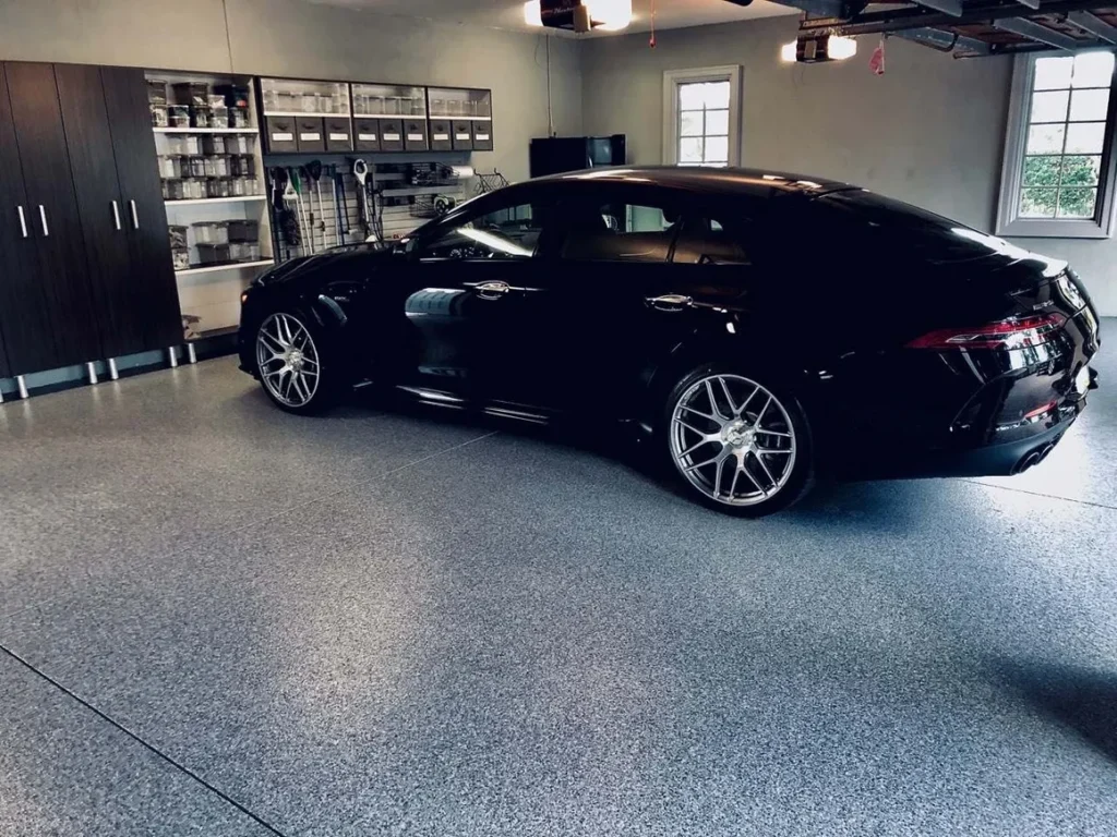 A black sedan is parked in a clean, organized garage with storage cabinets, shelves, and a window on the side wall. The polished concrete flooring adds a sleek, modern touch to the space. - Floor Coating Specialist - Bradenton, FL
