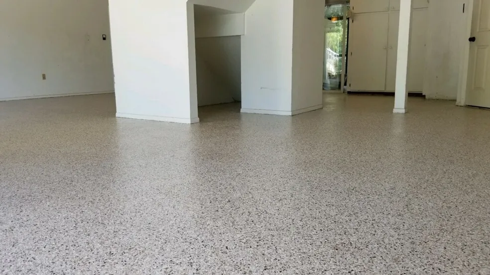 A room with white walls and a speckled epoxy floor coating, featuring a structural column and a small alcove under a staircase. - Floor Coating Specialist - Bradenton, FL
