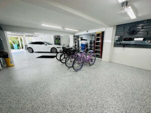Spacious garage with a white car, four bicycles, storage shelves, wall-mounted equipment, and a speckled epoxy floor. - Floor Coating Specialist - Bradenton, FL