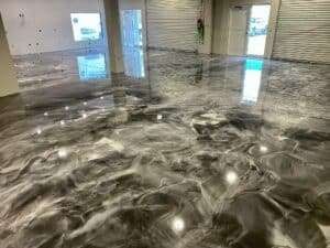 A polished, marbled epoxy floor with gray and white swirls reflects ceiling lights in an empty room with large windows and metal shutters. - Floor Coating Specialist - Bradenton, FL