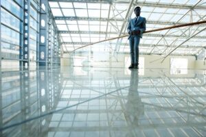 Man in a suit standing inside a modern glass building with metal beams and reflections on the shiny floor. - Floor Coating Specialist - Bradenton, FL