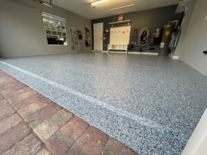 Clean garage with gray speckled epoxy floor, organized shelves, cleaning tools, and water heaters along the back wall, viewed from the entrance. - Floor Coating Specialist - Bradenton, FL