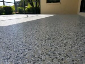 Close-up view of a newly coated epoxy garage floor with a speckled gray and white finish in a sunlit indoor space. - Floor Coating Specialist - Bradenton, FL